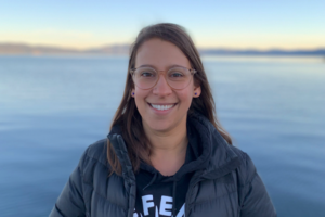 Smiling woman standing in front of large body of water.