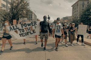 people marching together on a street, holding a sign that reads "All Power To The People"