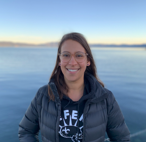 Smiling woman standing in front of large body of water.