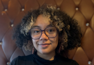 Woman with curly hair and glasses smiling at the camera.