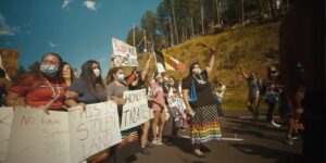 A group of people in masks at a #landback protest holding signs