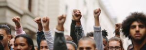 A group of people standing in the street with their hands raised in the air and forming fists in an act of encouragement and solidarity