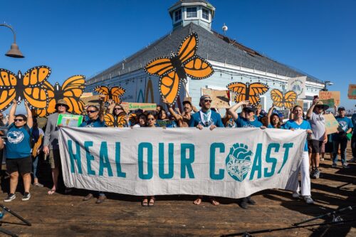 Group at San Diego / Tijuana border beach holding butterflies and a sign