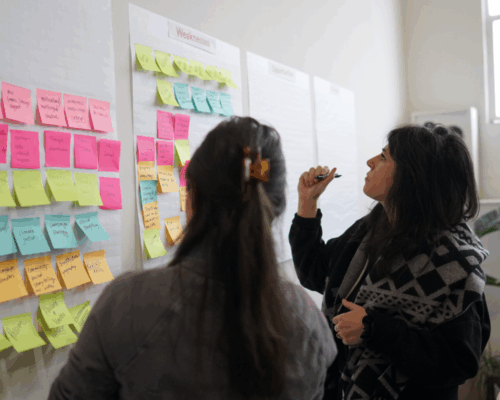 Two women looking at a whiteboard of sticky notes.